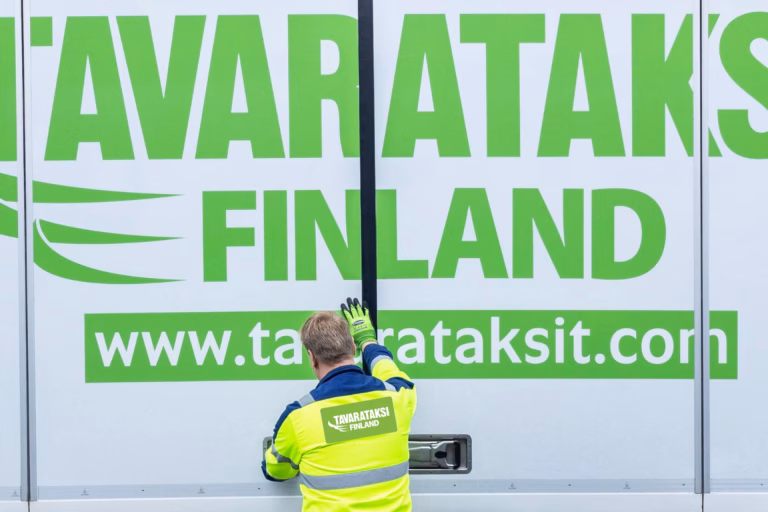 Kuva Tavarataksin autosta, jonka kylkeä kuljettaja on sulkemassa.